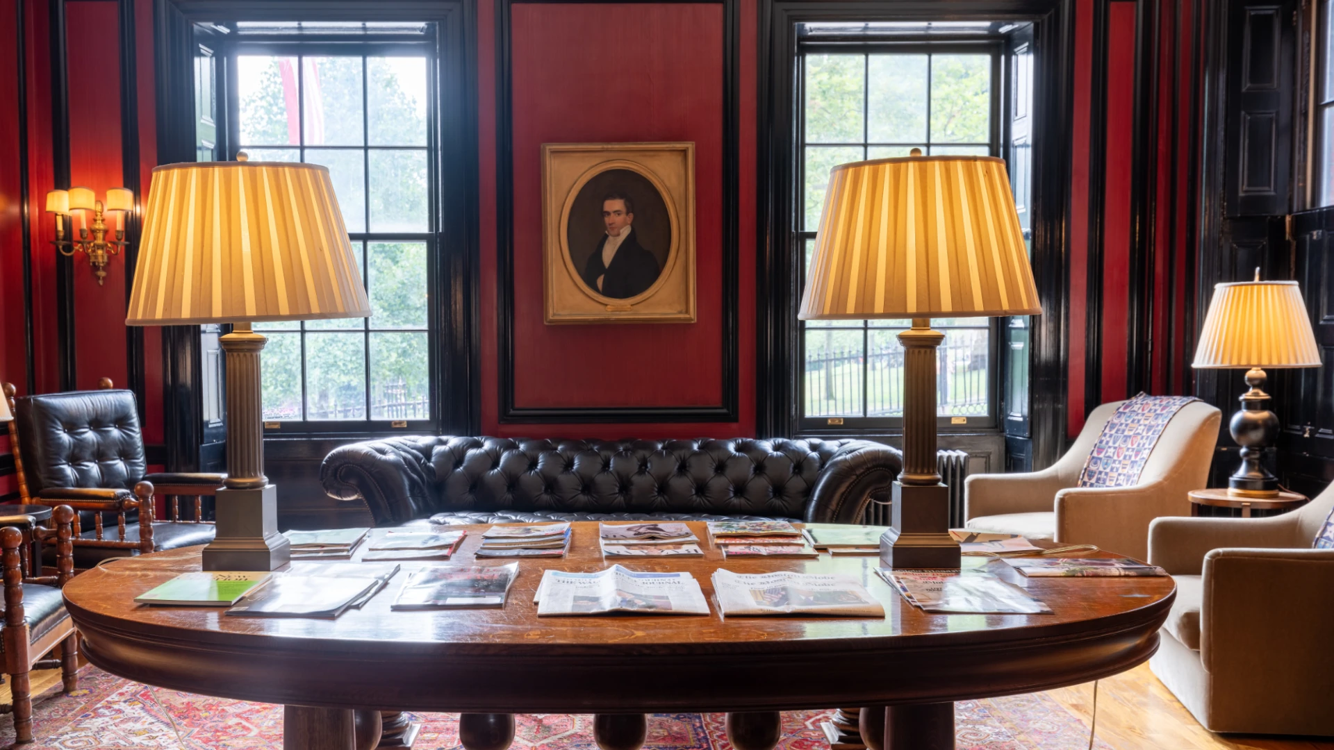 A table with ornate lamps foregrounds a sitting room of dark mahogany and reds.