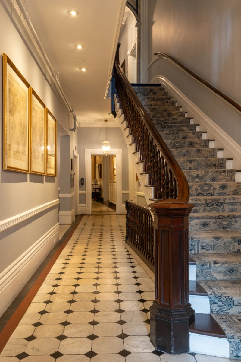 A staircase with blue carpet runs up a long tiled hallway.