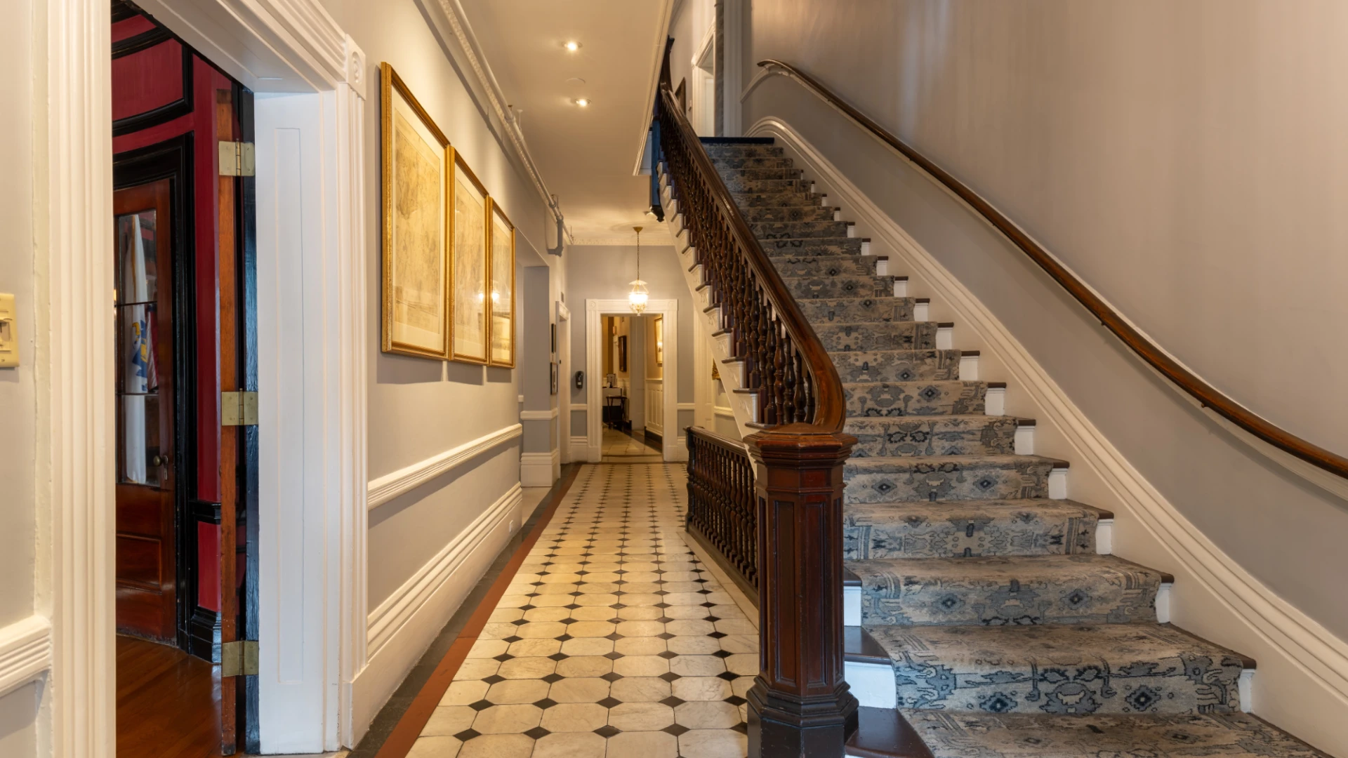A staircase with blue carpet runs up a long tiled hallway.