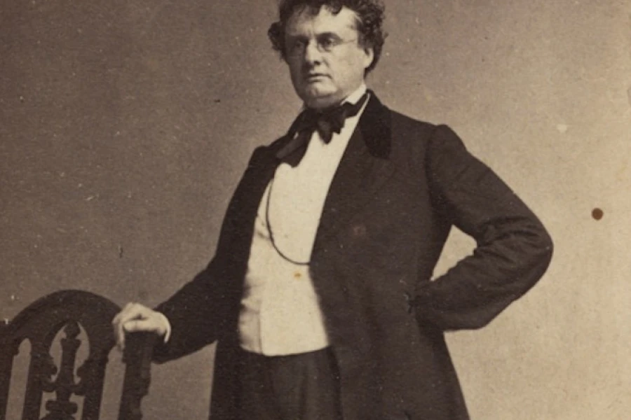 Antique photo portrait of Governor Andrew - a suited man stands next to a chair.