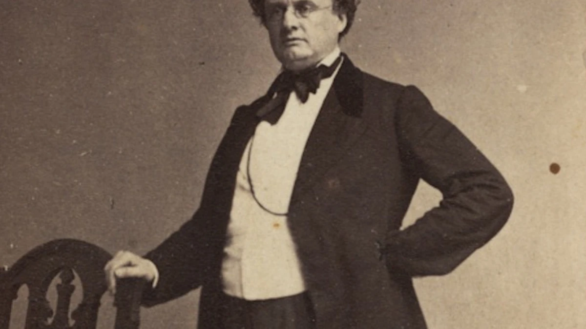 Antique photo portrait of Governor Andrew - a suited man stands next to a chair.