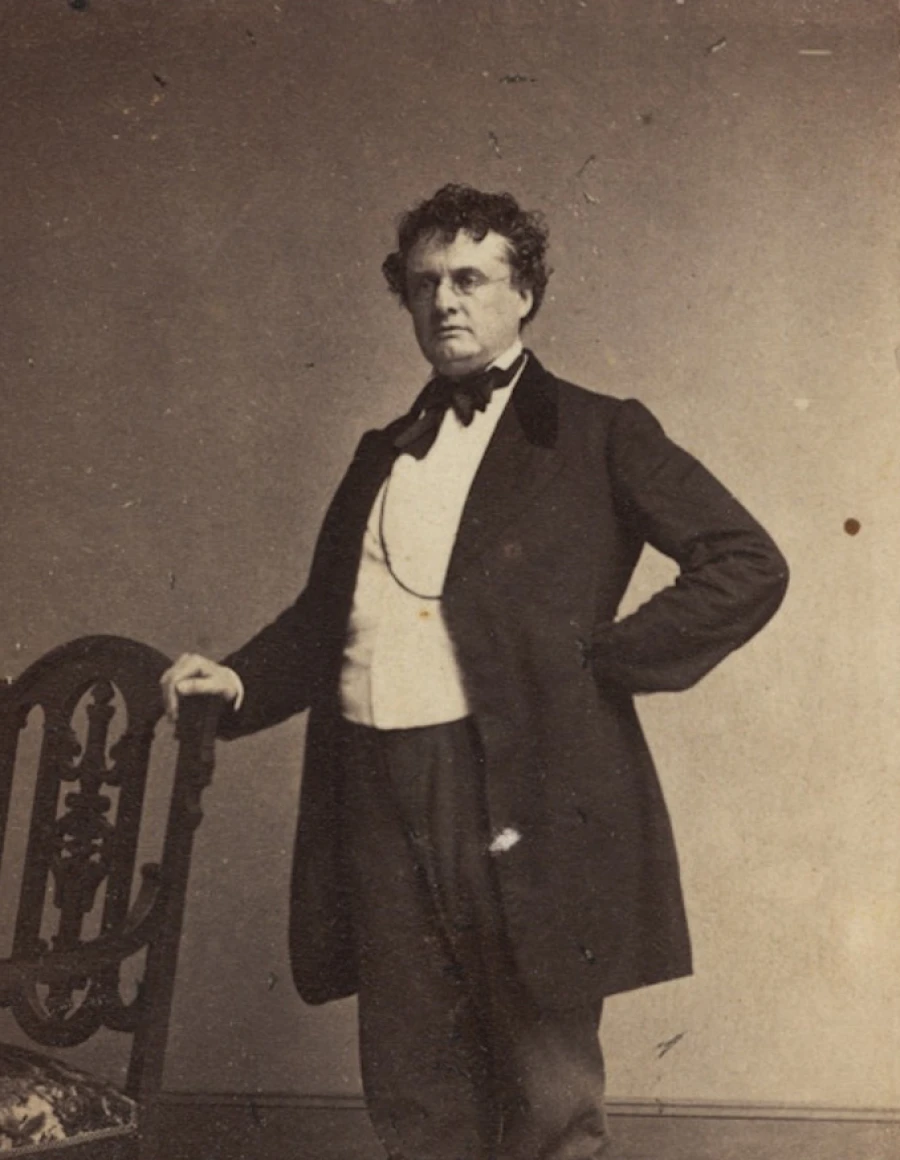 Antique photo portrait of Governor Andrew - a suited man stands next to a chair.